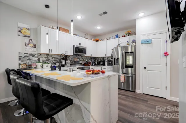 a kitchen with stainless steel appliances a sink a stove a refrigerator cabinets and a dining table with wooden floor