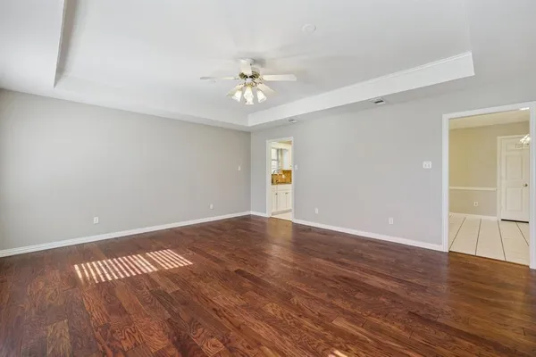 a view of an empty room with wooden floor and a ceiling fan