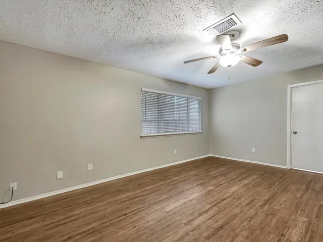 an empty room with wooden floor fan and windows