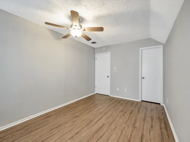 an empty room with wooden floor fan and windows