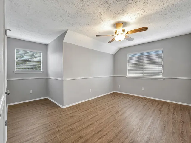 an empty room with wooden floor chandelier fan and windows
