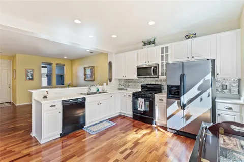 a kitchen with stainless steel appliances granite countertop a stove top oven a sink dishwasher a refrigerator and a dining table with wooden floor