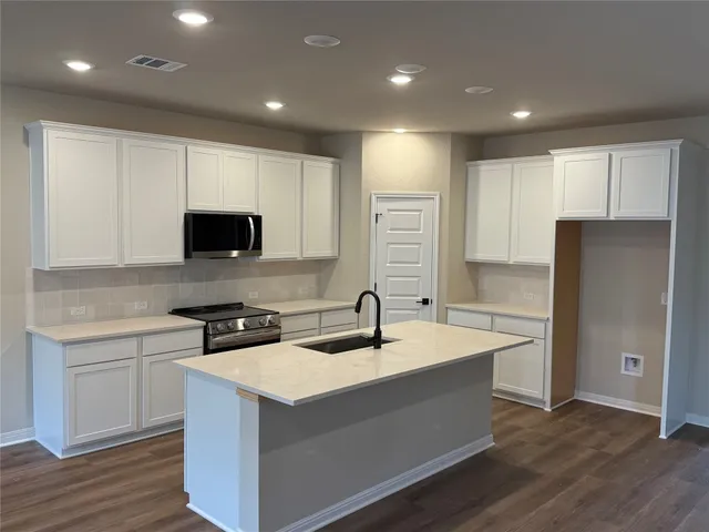 a kitchen with stainless steel appliances granite countertop a sink a microwave a refrigerator and white cabinets with wooden floor