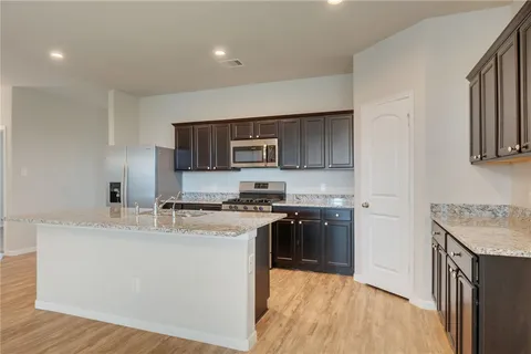 a kitchen with stainless steel appliances granite countertop a stove top oven a sink a refrigerator and white cabinets with wooden floor