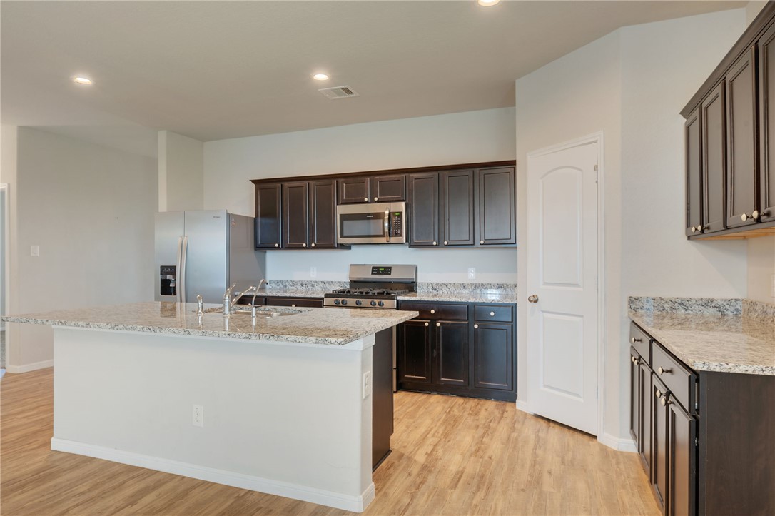 1700 Eagle View Drive Navasota, TX 77868 - Photo 4 of 22 a kitchen with stainless steel appliances granite countertop a stove top oven a sink a refrigerator and white cabinets with wooden floor