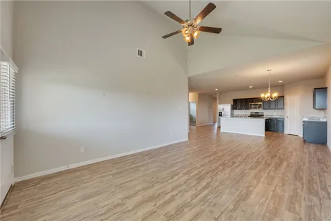 an empty room with wooden floor a kitchen view and a ceiling fan
