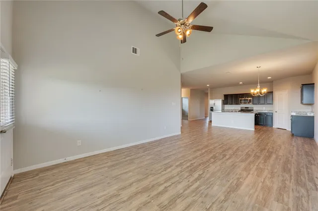 an empty room with wooden floor a kitchen view and a ceiling fan