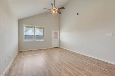 an empty room with wooden floor chandelier fan and windows