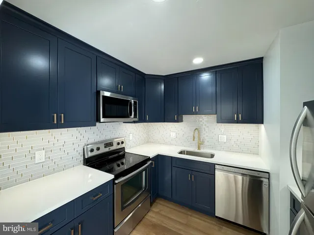 a kitchen with stainless steel appliances a sink dishwasher a stove top oven a refrigerator with wooden floor and cabinets