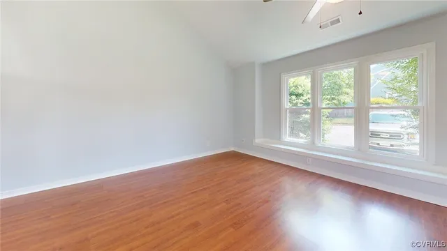 a view of an empty room with wooden floor and a ceiling fan