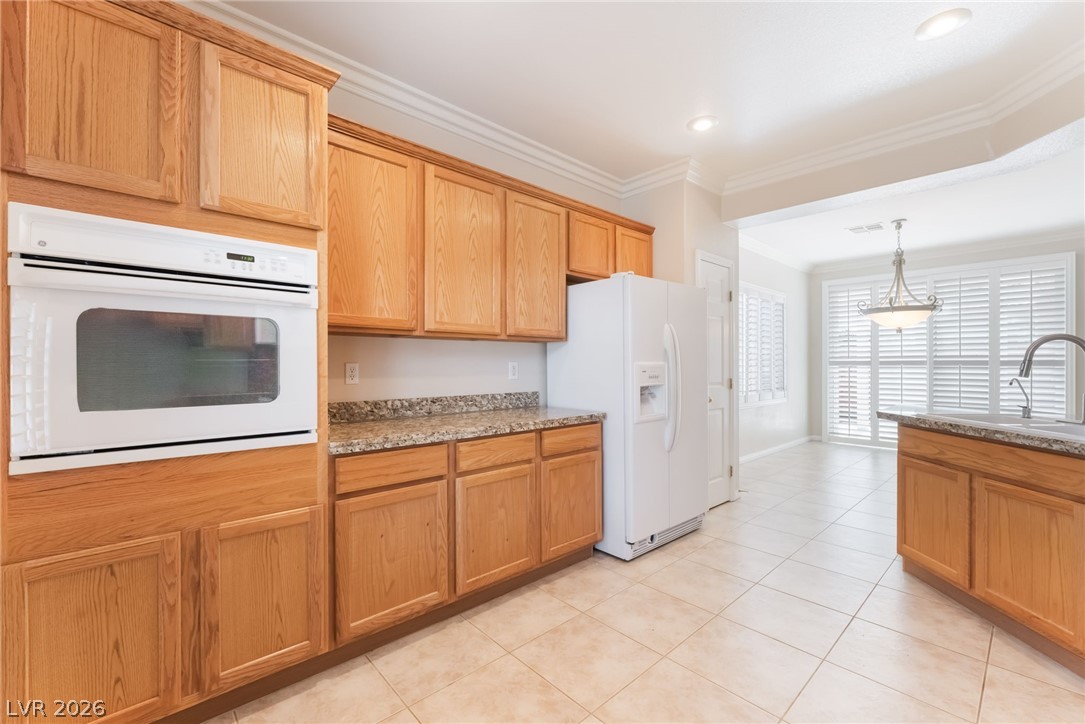 10481 Riverside Park Avenue Las Vegas, NV 89135 - Photo 16 of 51 Kitchen with white appliances, crown molding, hanging light fixtures, light tile patterned floors, and light stone countertops