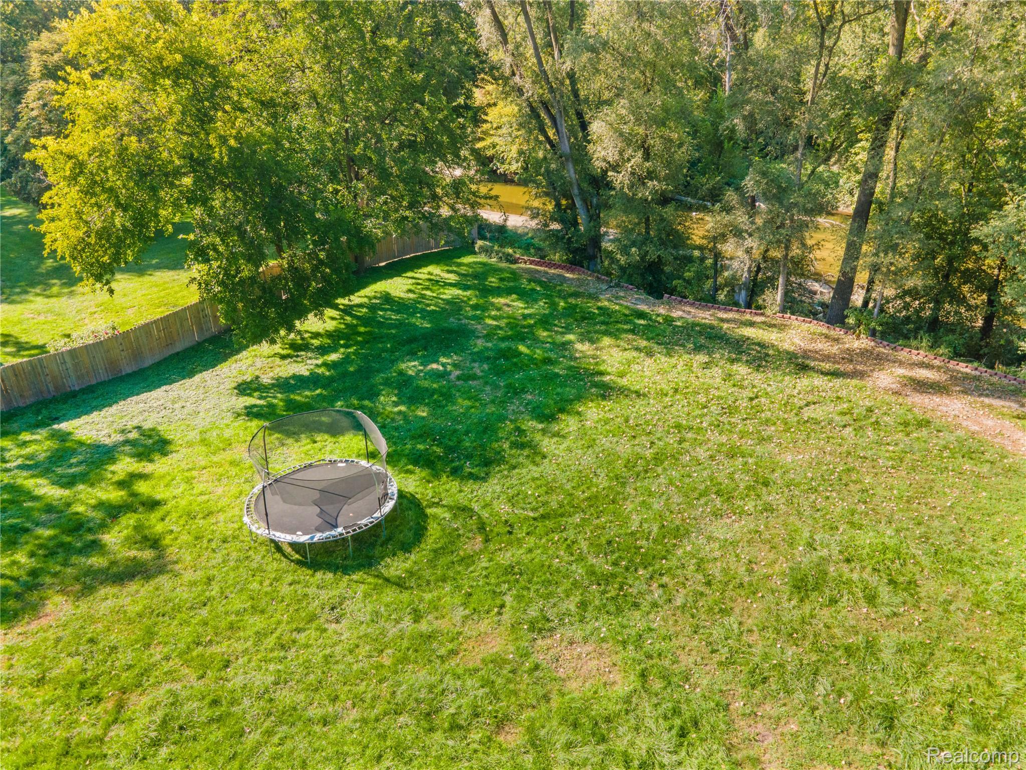 15879 Millar Road Clinton Township, MI 48036 - Photo 48 of 65 Expansive grass lawn with a wood fence, mature trees, and natural landscaping by the water