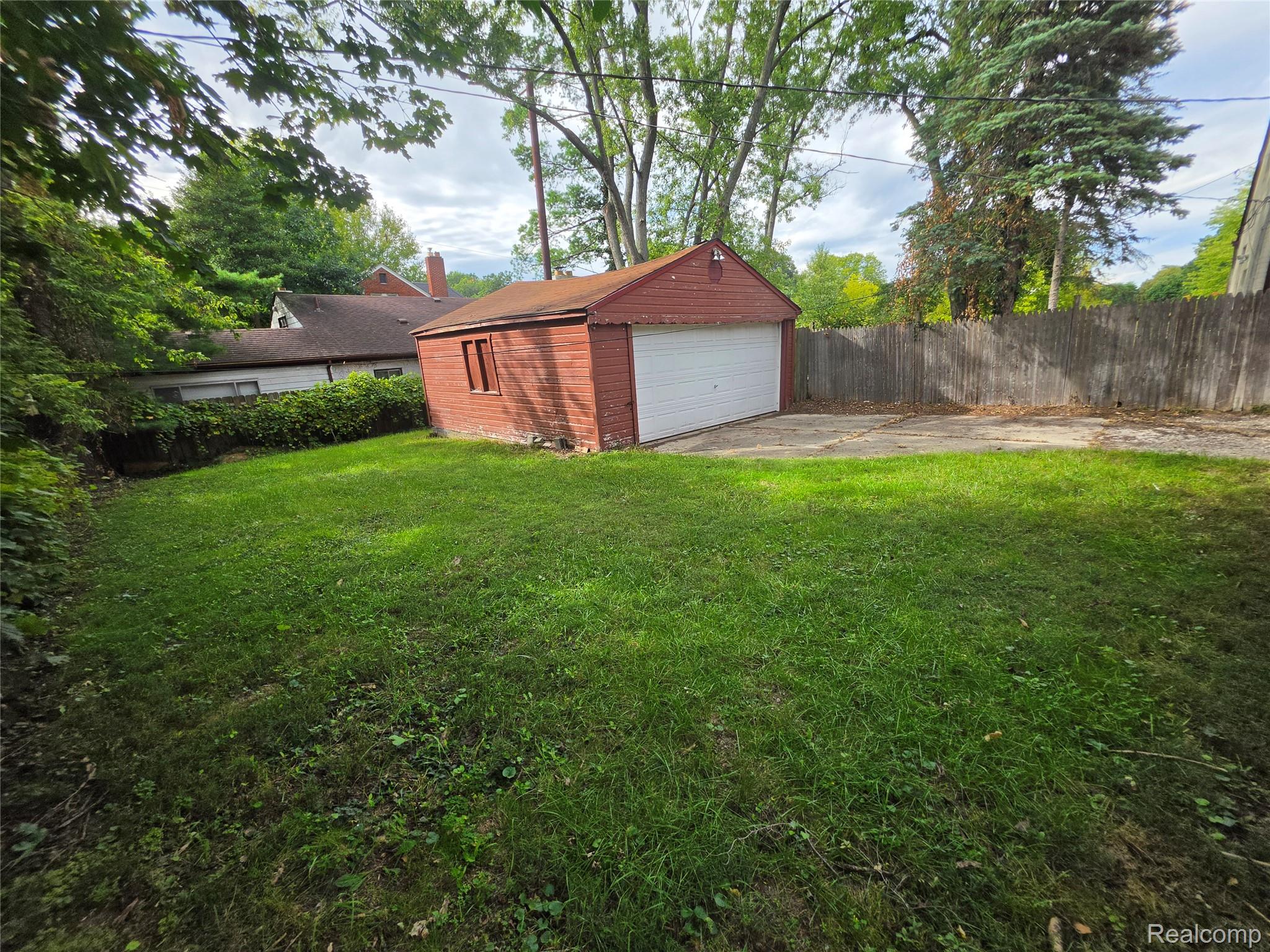 18539 Lahser Road Detroit, MI 48219 - Photo 22 of 23 Expansive grassy yard with mature trees, a red detached garage, and a wood privacy fence