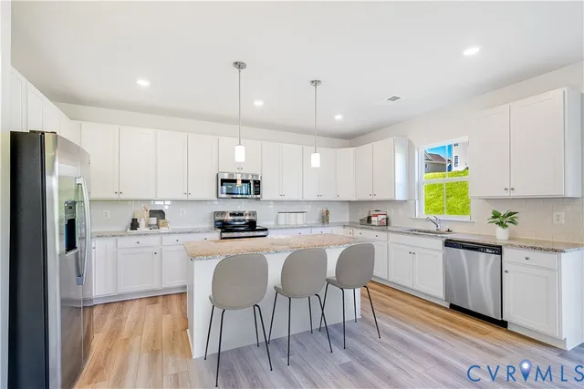 a kitchen with stainless steel appliances granite countertop white cabinets a sink dishwasher a stove and a refrigerator with wooden floor