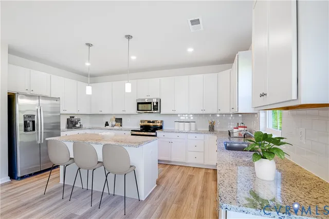 a kitchen with stainless steel appliances a dining table chairs stove refrigerator and cabinets