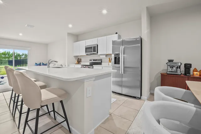 a kitchen with stainless steel appliances a refrigerator a sink a stove a dining table and chairs with wooden floor