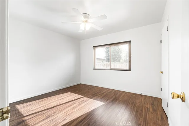 an empty room with wooden floor chandelier fan and windows