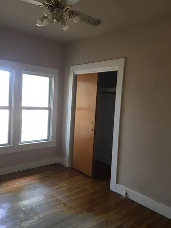 a view of an empty room with wooden floor and a ceiling fan