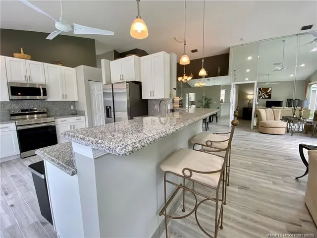 a kitchen with stainless steel appliances kitchen island granite countertop a refrigerator a stove a sink a dining table and chairs with wooden floor
