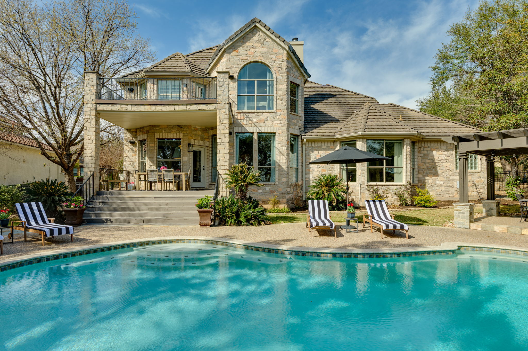 Rear view of house featuring stone siding, an outdoor pool, a patio, and a balcony