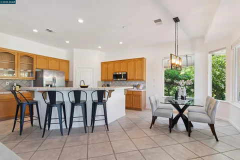 a kitchen with stainless steel appliances granite countertop a stove top oven a refrigerator a sink and a dining table with white cabinets