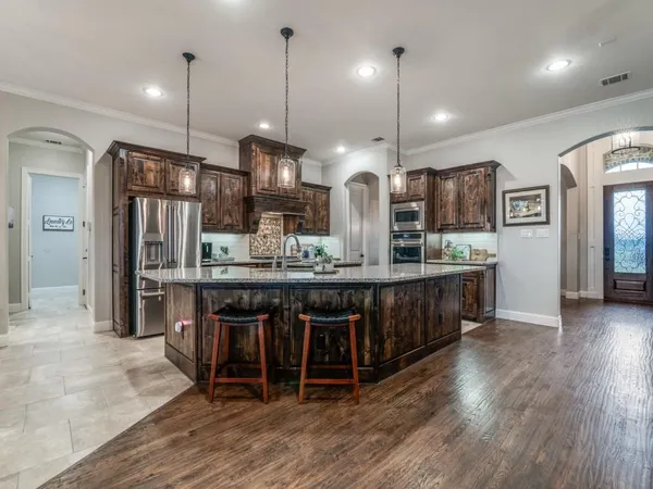 a kitchen with stainless steel appliances kitchen island granite countertop a refrigerator a oven a sink and a wooden floors