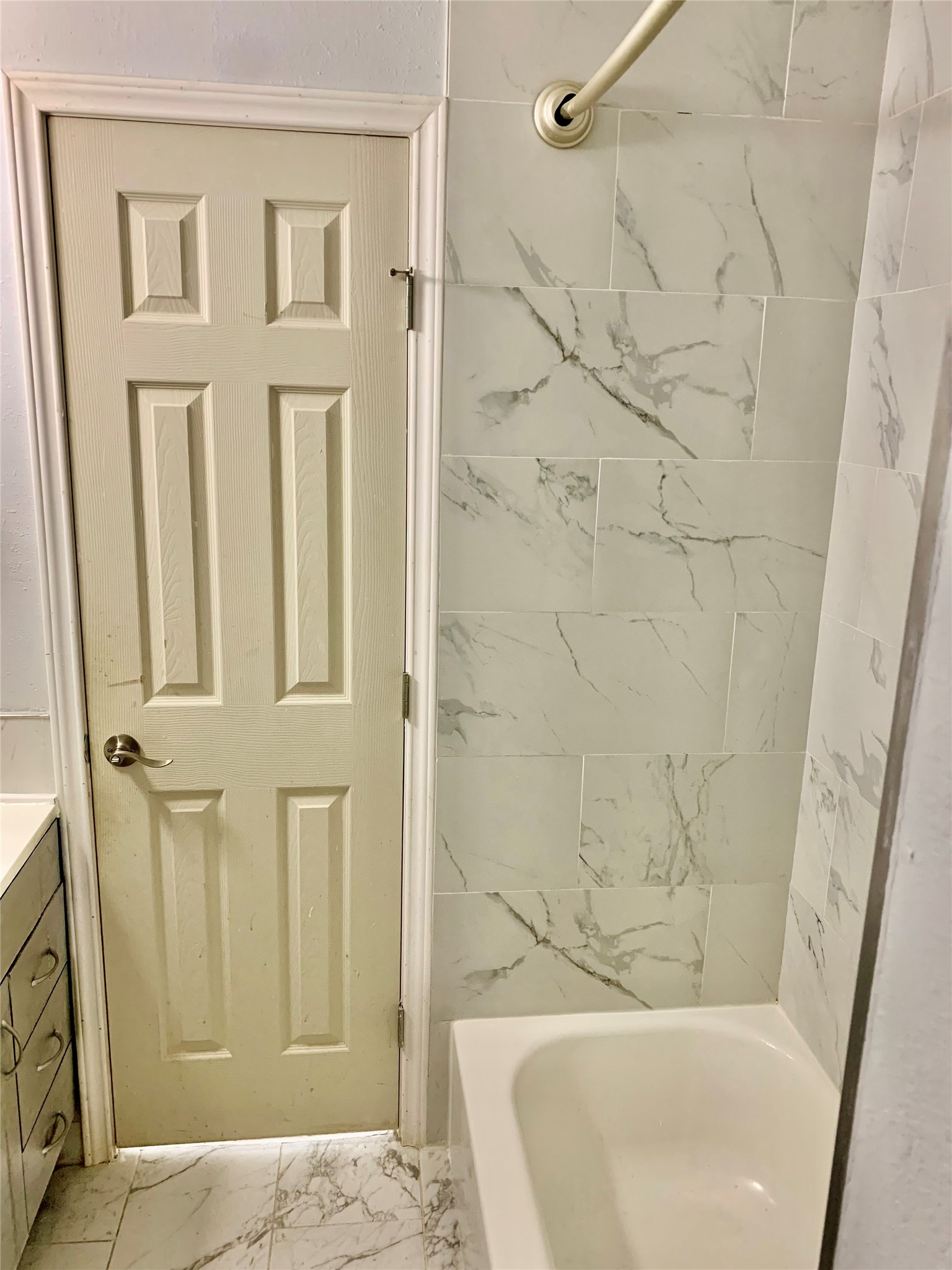 909 Silber Road, Unit 57J Houston, TX 77024 - Photo 11 of 14 This bathroom features a clean, modern design with a white marble-look tiled shower and bathtub. It includes a paneled door and adjacent vanity with drawers for storage.