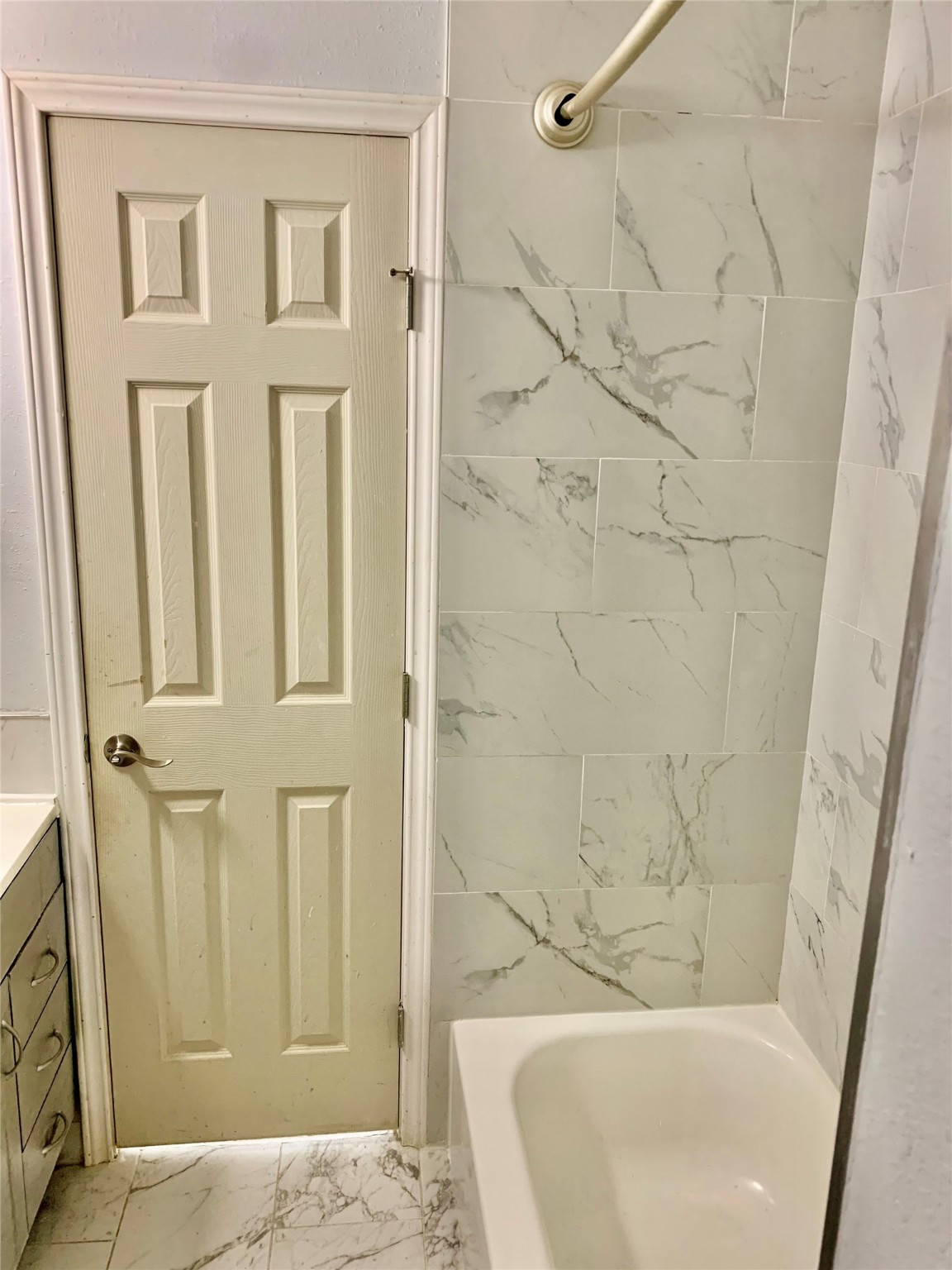 909 Silber Road, Unit 57J Houston, TX 77024 - Photo 11 of 14 This bathroom features a clean, modern design with a white marble-look tiled shower and bathtub. It includes a paneled door and adjacent vanity with drawers for storage.