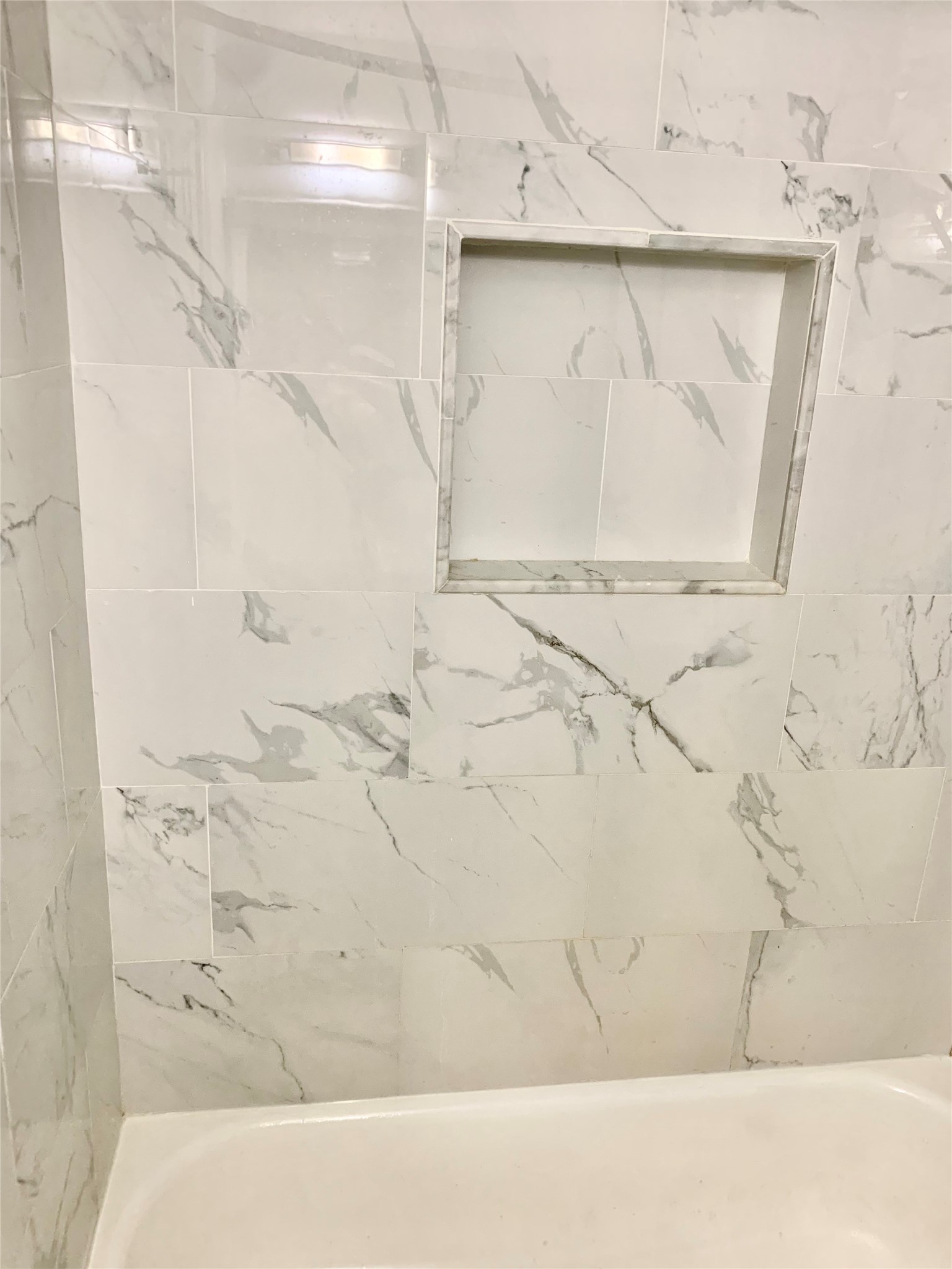 909 Silber Road, Unit 57J Houston, TX 77024 - Photo 12 of 14 This bathroom features elegant, white marble-patterned tiles with a built-in shower niche for convenient storage. The clean design adds a touch of sophistication.