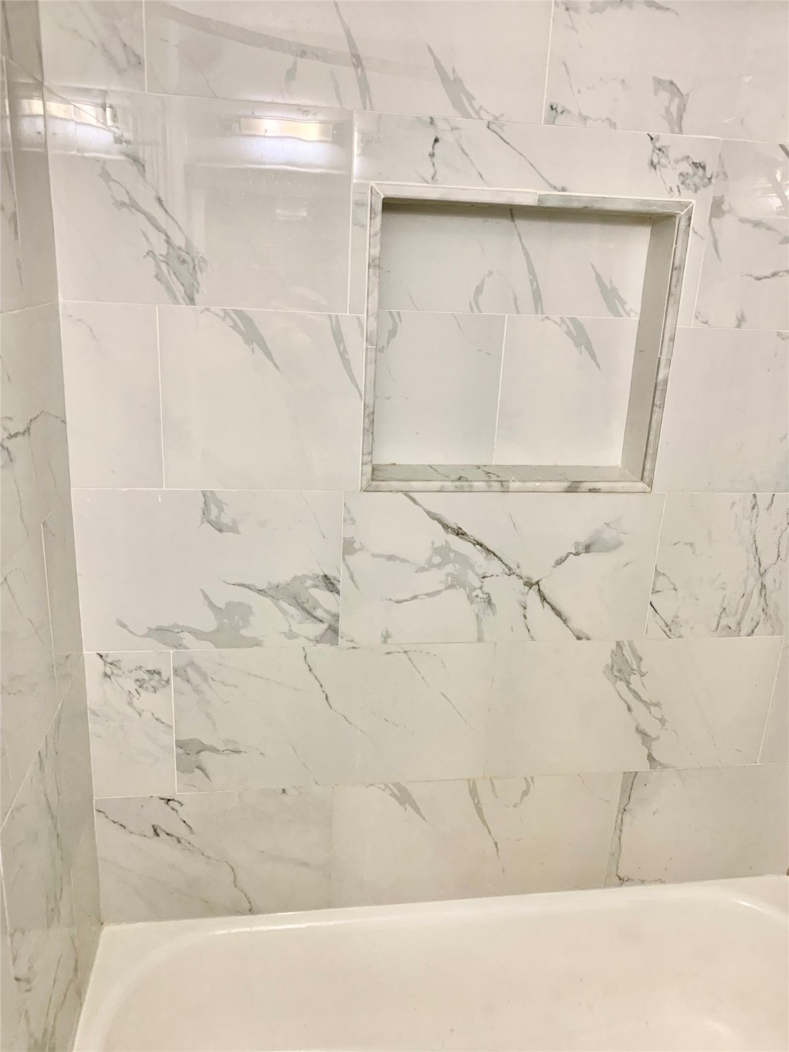 909 Silber Road, Unit 57J Houston, TX 77024 - Photo 12 of 14 This bathroom features elegant, white marble-patterned tiles with a built-in shower niche for convenient storage. The clean design adds a touch of sophistication.