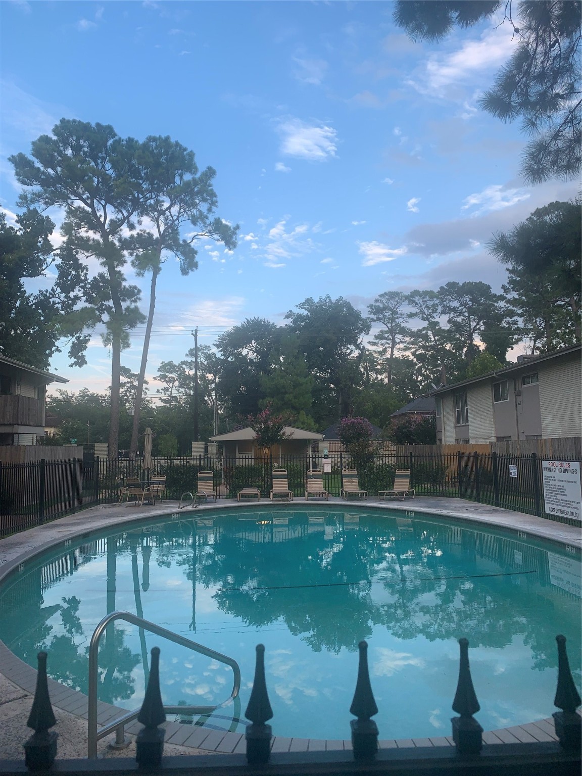 909 Silber Road, Unit 57J Houston, TX 77024 - Photo 14 of 14 This photo showcases a charming residential area with a circular swimming pool, surrounded by a secure fence and lounge chairs. The area is lush with tall trees, offering a serene and inviting atmosphere.