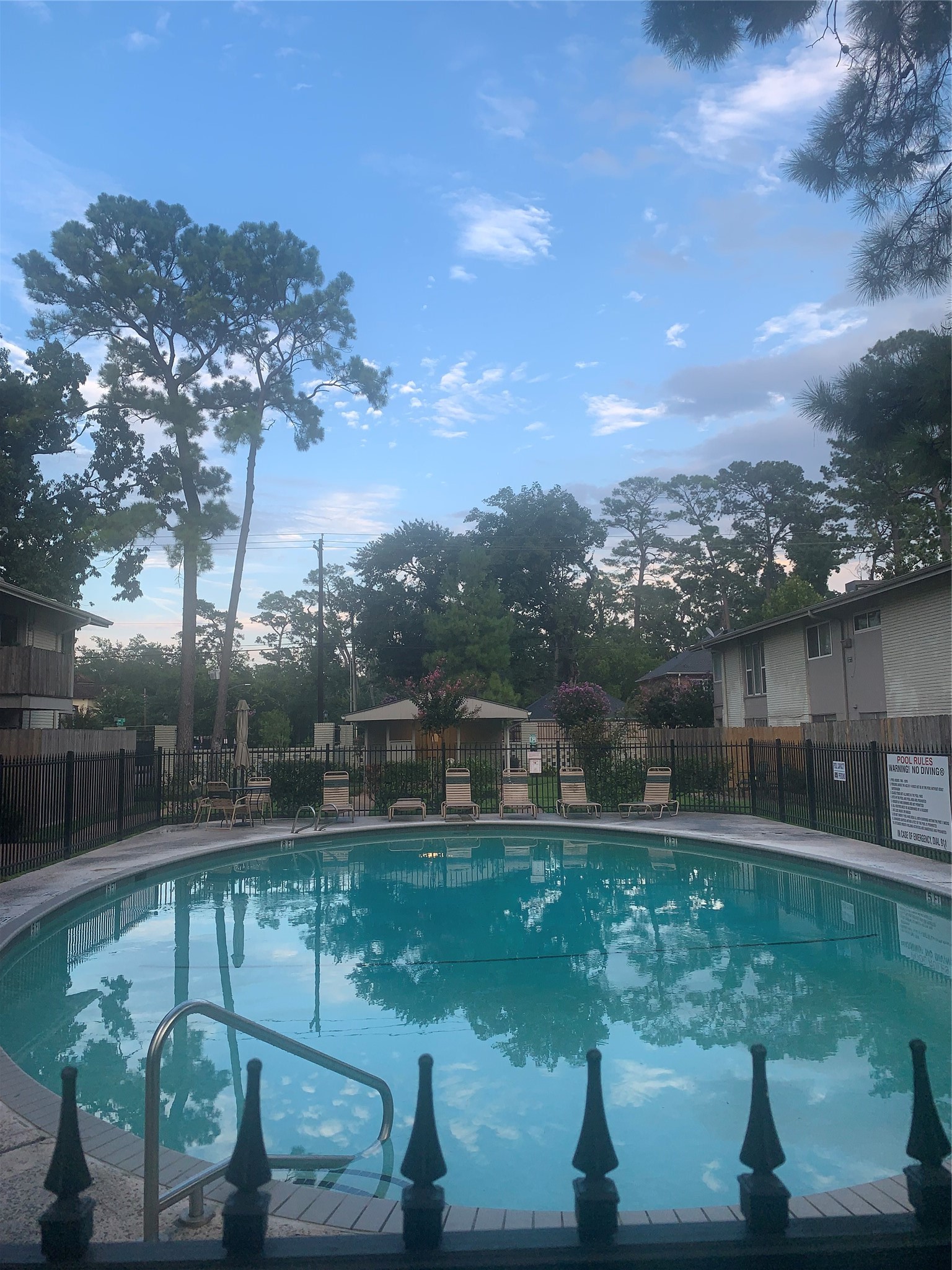 909 Silber Road, Unit 57J Houston, TX 77024 - Photo 14 of 14 This photo showcases a charming residential area with a circular swimming pool, surrounded by a secure fence and lounge chairs. The area is lush with tall trees, offering a serene and inviting atmosphere.