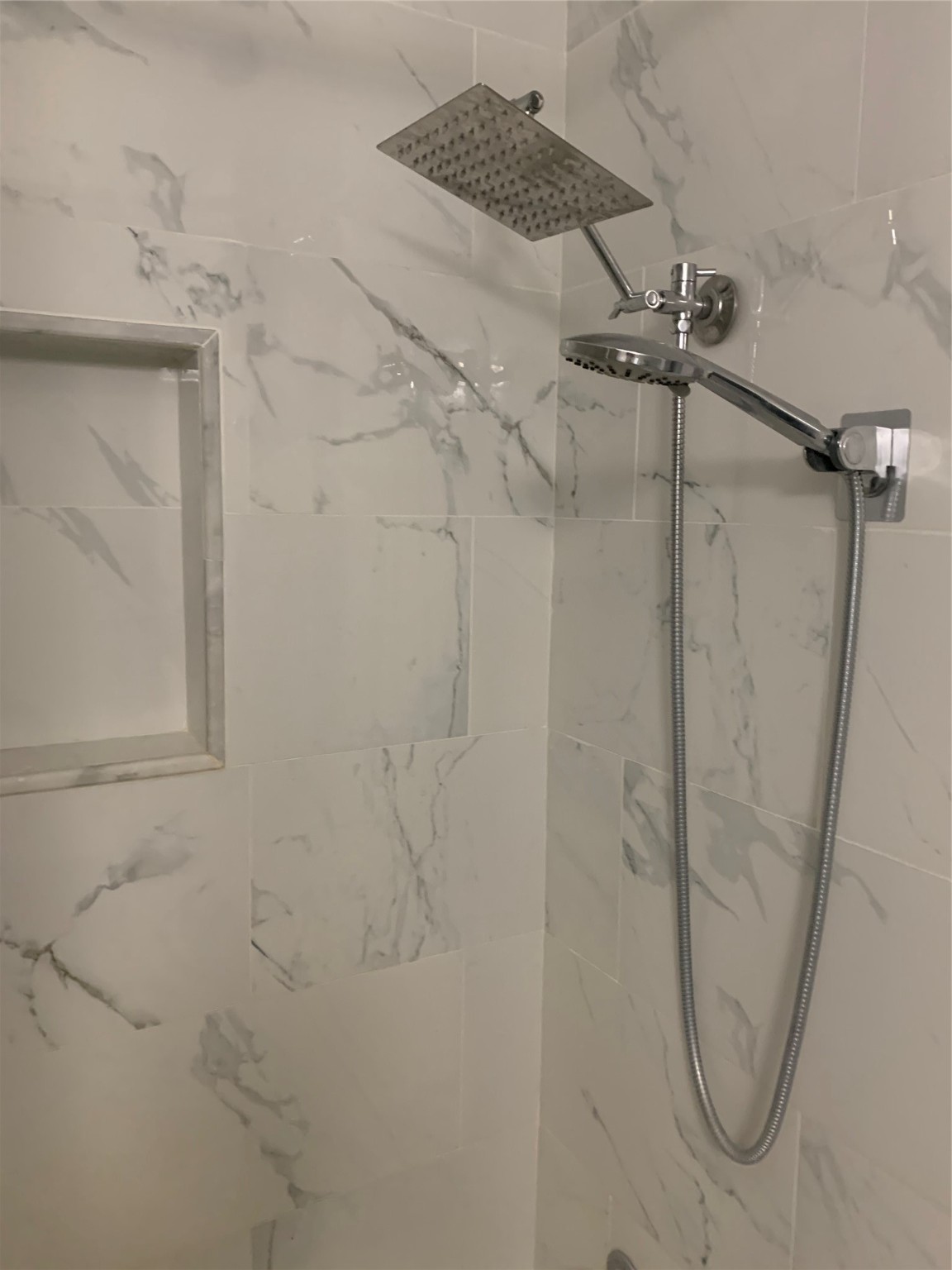 909 Silber Road, Unit 57J Houston, TX 77024 - Photo 10 of 14 This bathroom features a modern shower with a sleek rainfall showerhead and elegant marble-patterned tiles, along with a convenient built-in shelf.