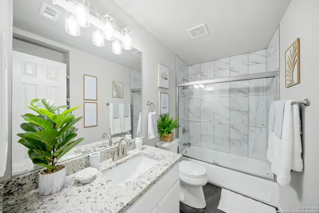 a bathroom with a granite countertop sink a toilet a large mirror and shower