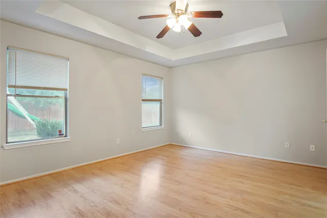 an empty room with wooden floor chandelier fan and windows