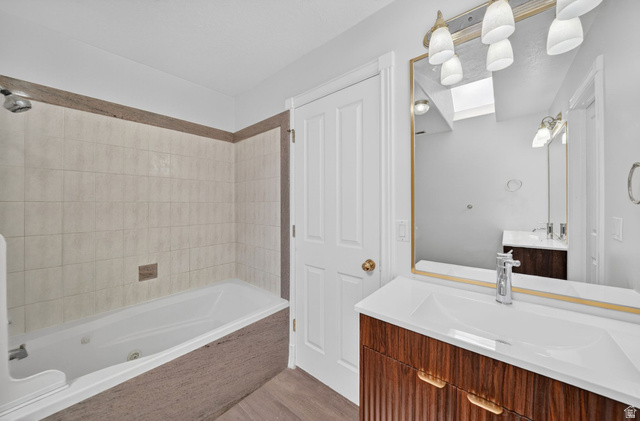 883 East 700 South Springville, UT 84663 - Photo 31 of 59 Bathroom featuring a built-in tub with tile surround, a wood-finish vanity with an integrated sink, a rectangular framed mirror, and a multi-bulb light fixture