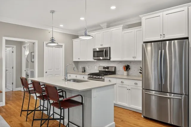 a kitchen with stainless steel appliances a refrigerator a stove a sink a dining table and chairs with wooden floor