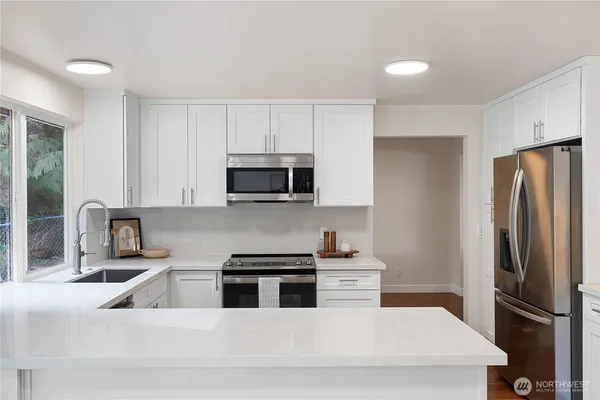 a kitchen with stainless steel appliances granite countertop a refrigerator a sink a stove a microwave and white cabinets