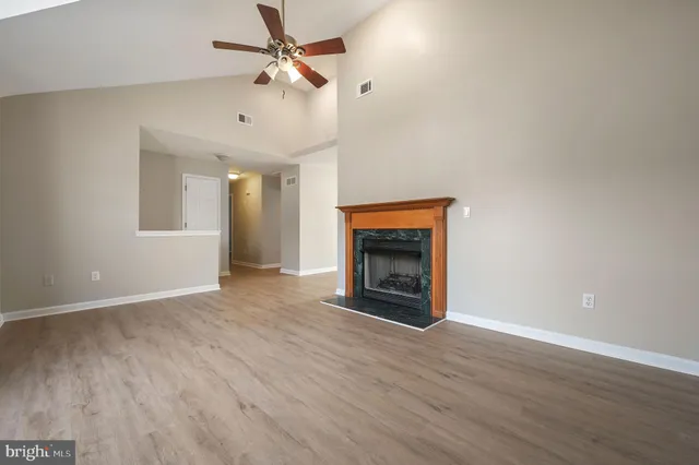 an empty room with wooden floor a fireplace a ceiling fan a kitchen and a window