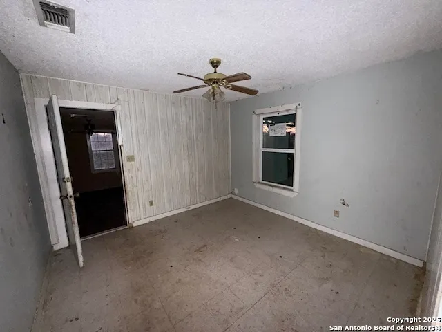 an empty room with chandelier fan and windows