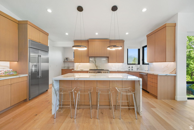 3667 Little Cottonwood Road, Unit 1 Sandy, UT 84092 - Photo 10 of 49 Gourmet kitchen featuring a large waterfall island with integrated seating, light wood-finish cabinetry, stainless steel appliances, and a full-height marble-style backsplash
