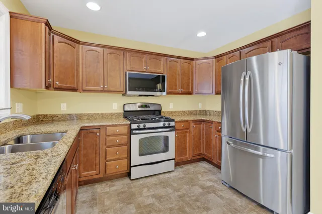 a kitchen with granite countertop stainless steel appliances a refrigerator stove top oven and sink