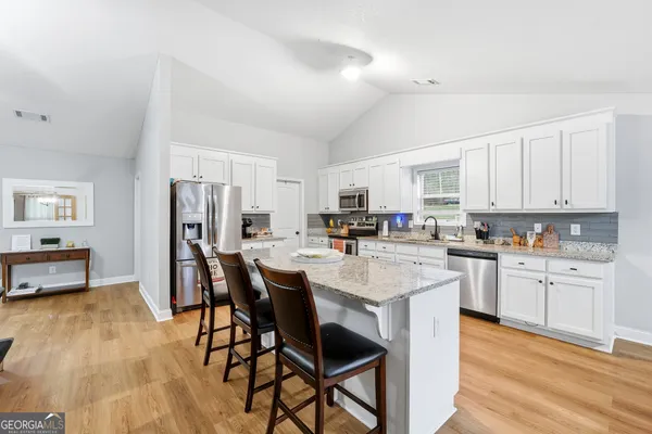 a kitchen with stainless steel appliances kitchen island a table chairs sink refrigerator and cabinets