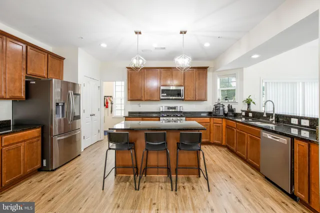 a kitchen with stainless steel appliances granite countertop a refrigerator a sink dishwasher a stove and white countertops with wooden floor