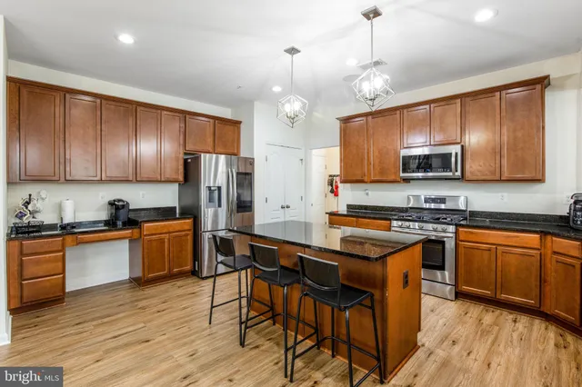 a kitchen with stainless steel appliances granite countertop wooden cabinets a refrigerator a stove a sink and dishwasher a oven with wooden floor
