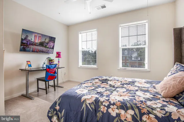 a bedroom with a bed a standing fan and a window