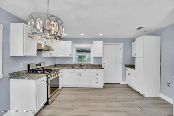 a large kitchen with stainless steel appliances granite countertop a white cabinets and chandelier