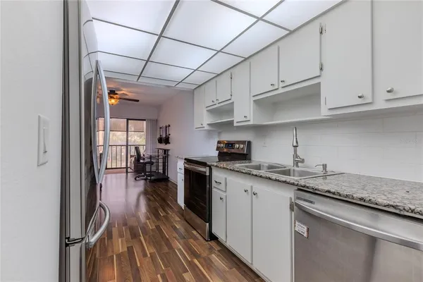 a kitchen with stainless steel appliances granite countertop a sink dishwasher a stove and white cabinets with wooden floor