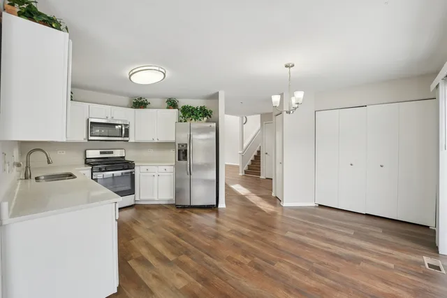 a kitchen with granite countertop a refrigerator oven a sink dishwasher and white cabinets with wooden floor