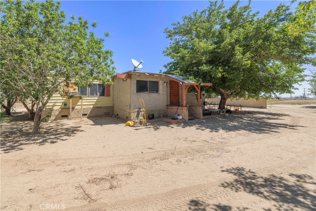 15374 Gaskell Road Rosamond, CA 93560 - Photo 25 of 74 a front view of a house with a dirt yard and a large tree